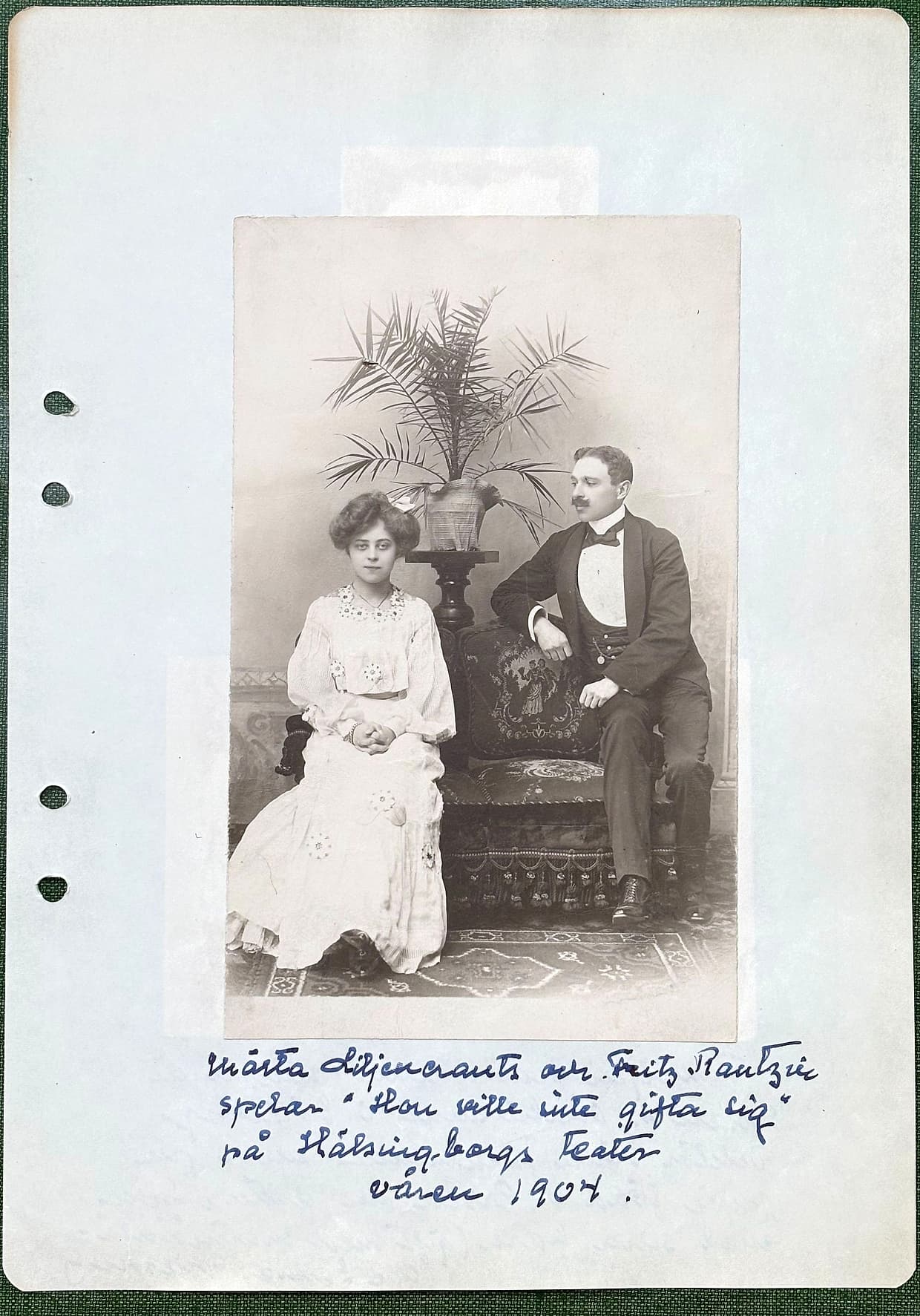 Fotograferad dagbokssida 111. Ett scenfotografi är inklistrat på arket: en ung kvinna i ljus klänning sitter, en man i frack står vid ett bord med en palm bakom sig. Märtas bildtext under fotografiet är återgiven under bilden.