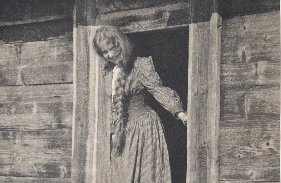 Märta, 21 år, i randig kjol och blus i dörröppningen till en timrad bod på Lilla Carlsö, midsommardagen 1905.